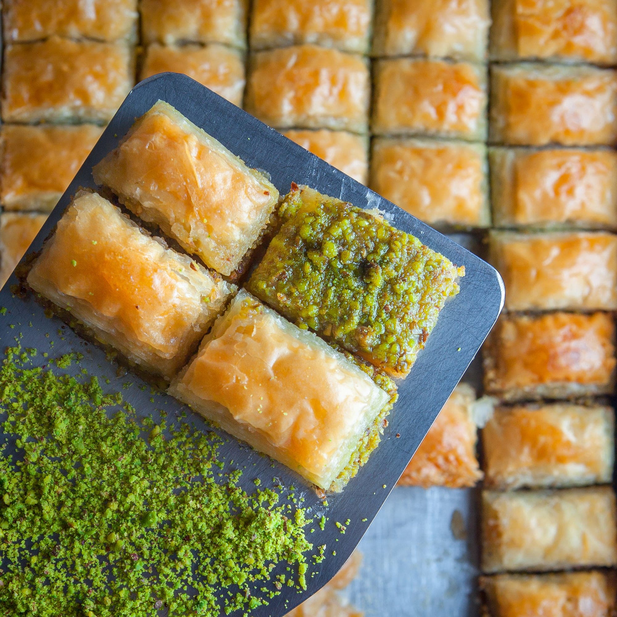 Tepsiden yeni kesilmiş fıstıklı ve sade baklava dilimleri, yanında öğütülmüş Antep fıstığı