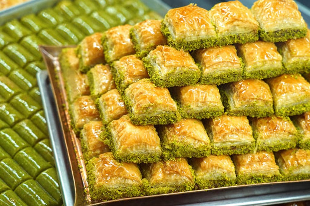 Tepside sıra sıra dizilmiş fıstıklı baklava dilimleri, yanında yeşil fıstık ezmeli sarma